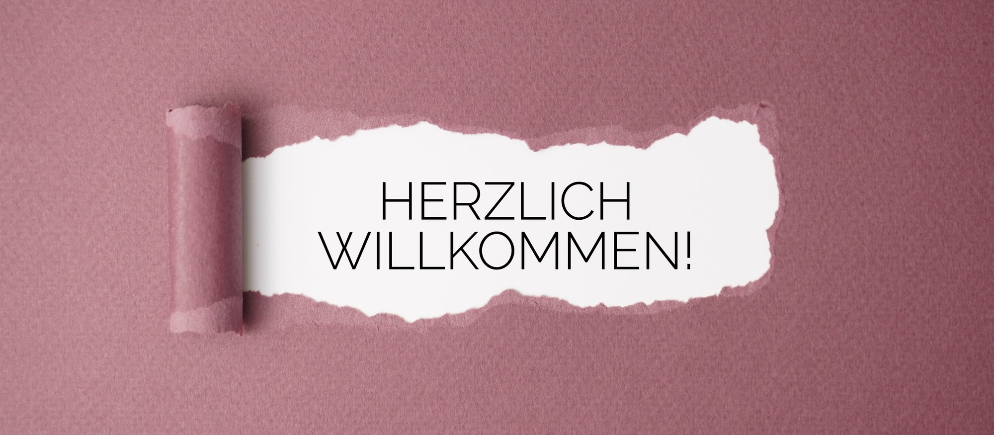 Aufgerissenes Papier mit dem Schriftzug Herzlich willkommen